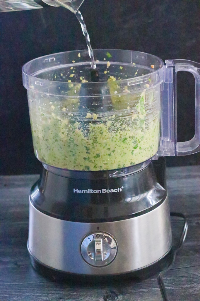 side shot of water being poured into a food processor for sauce and avocado