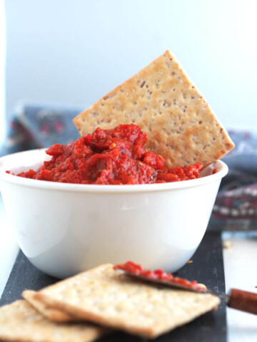 hot Serbian ajvar in a white bowl with a cracker in it.