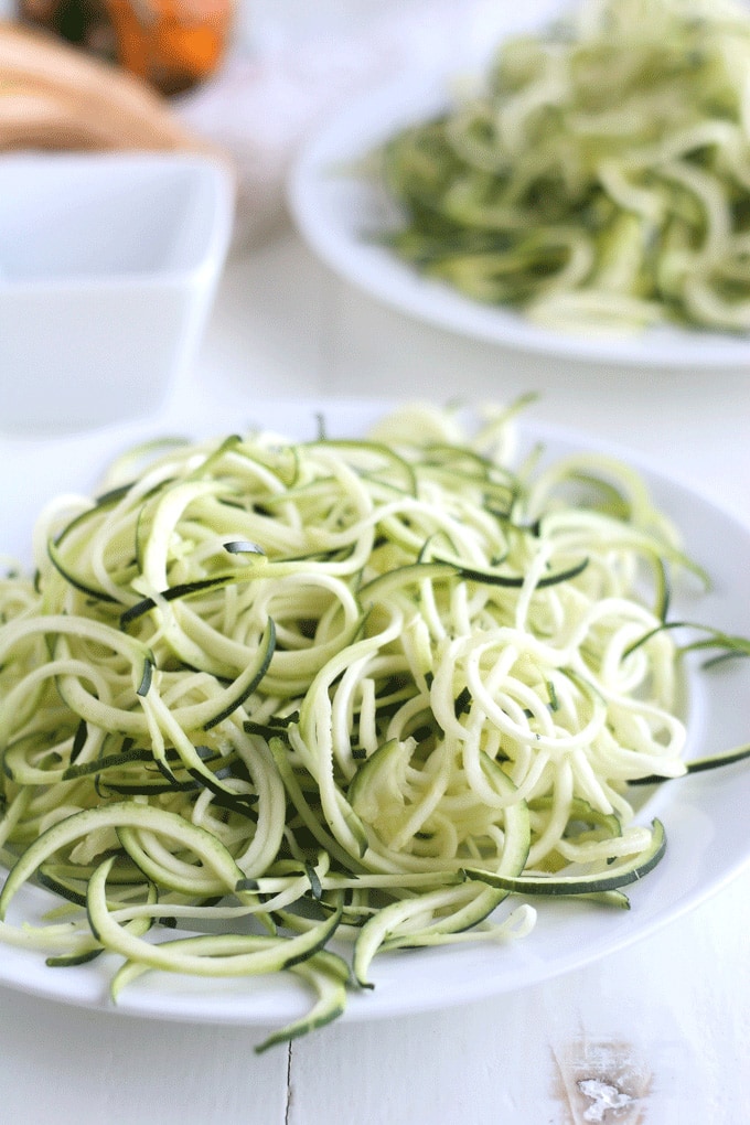 A plate of raw zucchini noodles on a white table