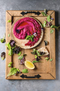 bowl of roasted beet hummus on cutting board with trimmings