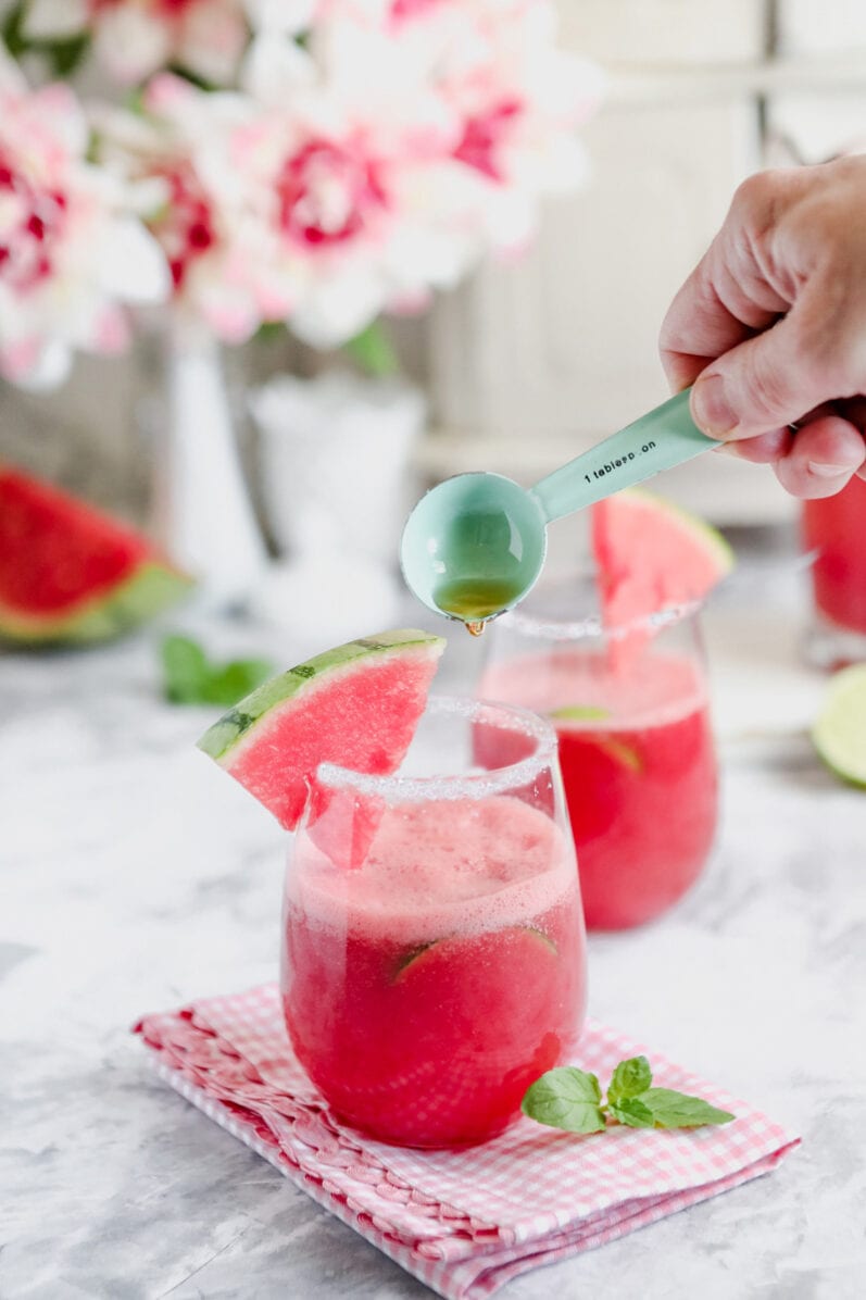 person pouring agave nectar in glass of watermelon agua fresca